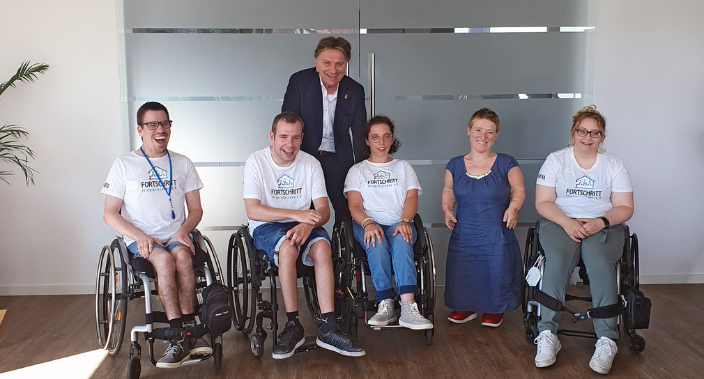 Minister Lucha und Simone Fischer zusammen mit vier Bewohnern und Bewohnerinnen der WG, die im Rollstuhl im sitzen.