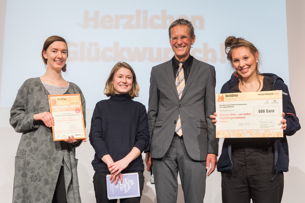 Gruppenfoto von Ministerialdirektor Wolf Hammann und drei jungen Frauen vom Projekt "girls for girls" auf der Bühne