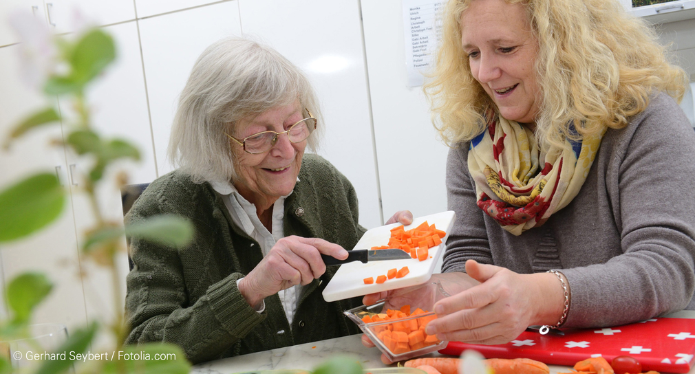 Frau hilft älterer Frau beim Gemüse schneiden