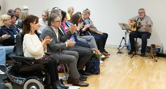 Musiker mit Gitarre spielt bei Veranstaltung vor Publikum.