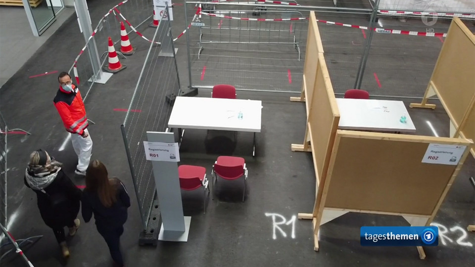 Drei Menschen laufen durch ein Impfzentrum