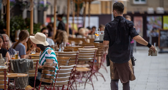 Eine Servicekraft läuft im Außenbereich eines Restaurants an Gästen vorbei.
