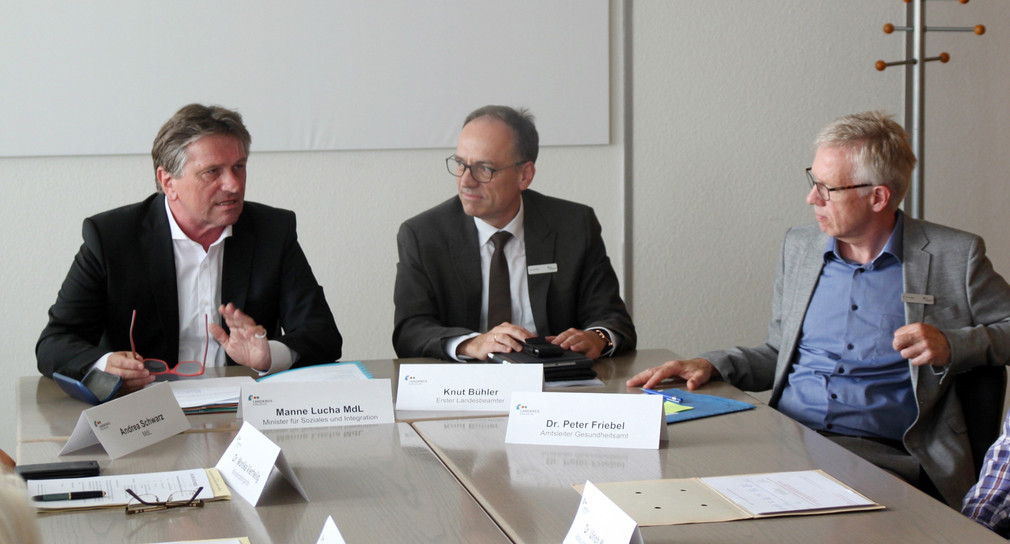 Minister Manne Lucha, Erster Landesbeamter Knut Bühler und Amtsleiter Dr. Peter Friebel vom Gesundheitsamt Karlsruhe sitzen gemeinsam an einem Besprechungstisch