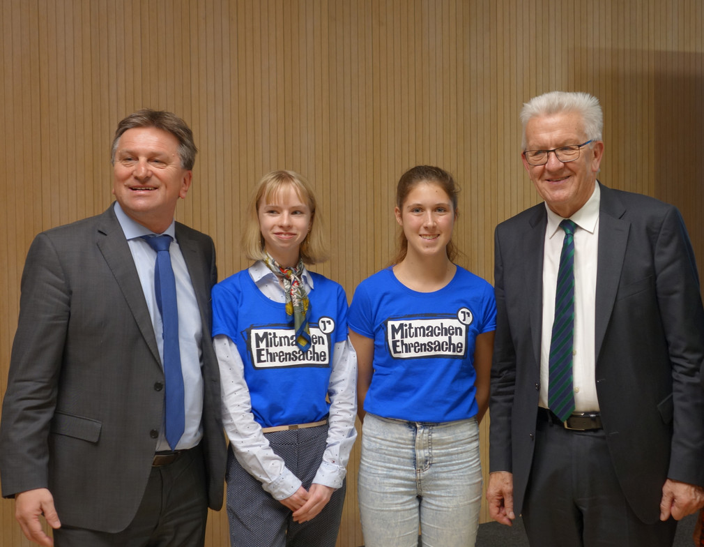 Gruppenfoto von zwei Schülerinnen mit Minister Manne Lucha und Ministerpräsident Winfried Kretschmann im Medienzentrum des Landtags von Baden-Württemberg