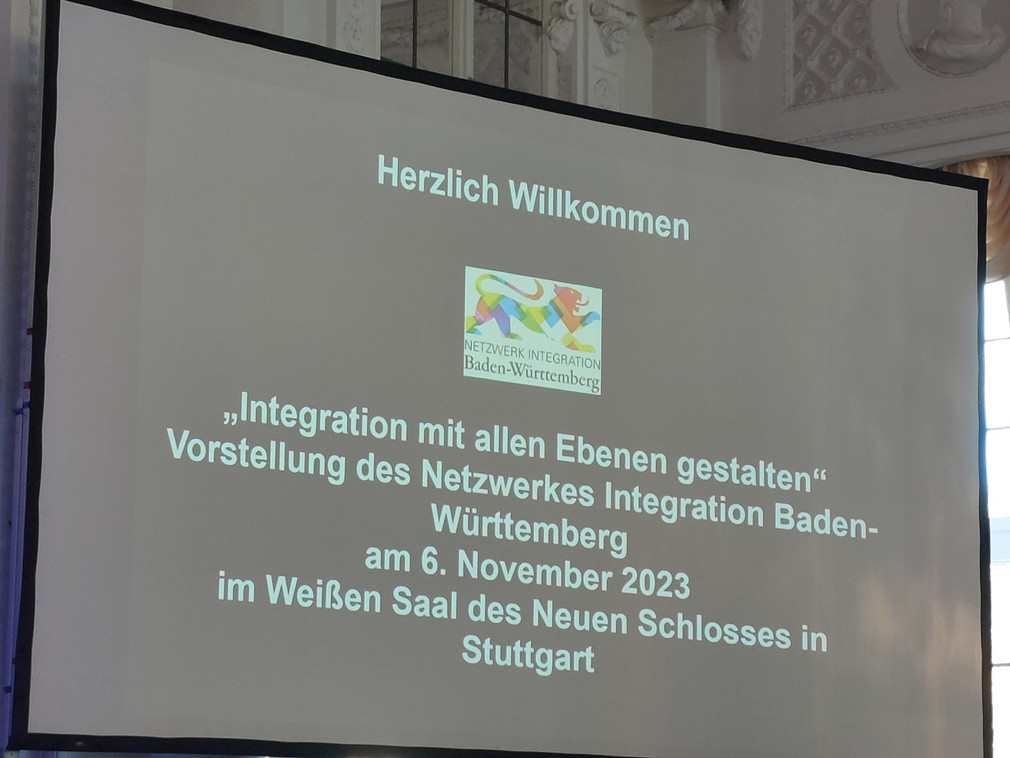 Leinwand auf Bühne zeigt Willkommensfolie mit Logo des Netzwerks Integration zur Netzwerkveranstaltung „Integration mit allen Ebenen gestalten“ am 6. November 2023 im Neuen Schloss in Stuttgart