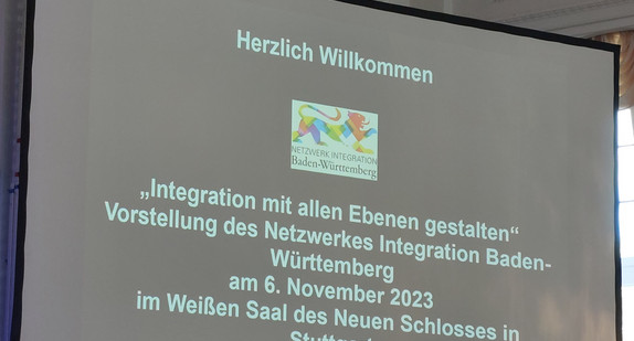 Leinwand auf Bühne zeigt Willkommensfolie mit Logo des Netzwerks Integration zur Netzwerkveranstaltung „Integration mit allen Ebenen gestalten“ am 6. November 2023 im Neuen Schloss in Stuttgart