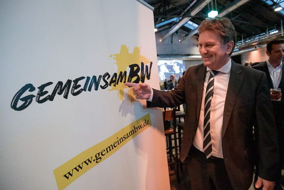 Sozial- und Integrationsminister Manne Lucha zeigt auf Roll-up mit dem Hashtag „gemeinsamBW“