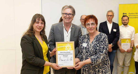 Sozialminister Manne Lucha posiert gemeinsam mit Preisträgern und ihrer Siegerurkunde.