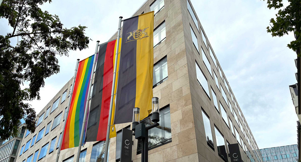 Vor dem Gebäude des Sozialministerium hängen nebeneinander eine Regenbogenflagge sowie die Flaggen von Deutschland und Baden-Württemberg.