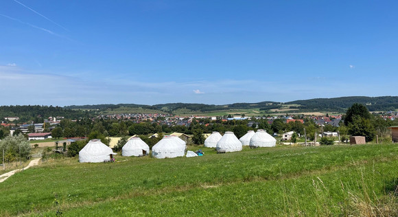 Blick aus der Ferne auf mehrere Jurten auf einer Wiese.