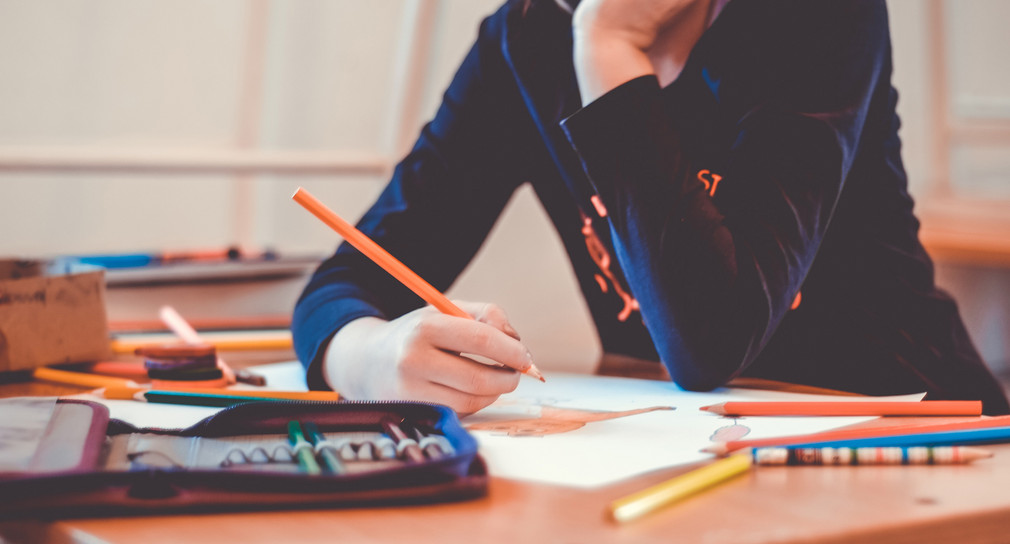 Schulkind malt in einem Heft, auf dem Tisch liegt ein Stiftemäppchen.