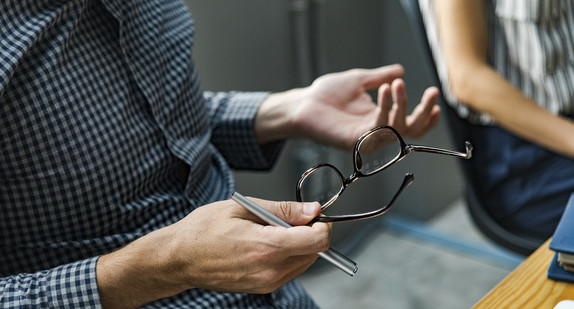 Mann spricht bei Besprechung mit Brille in der Hand