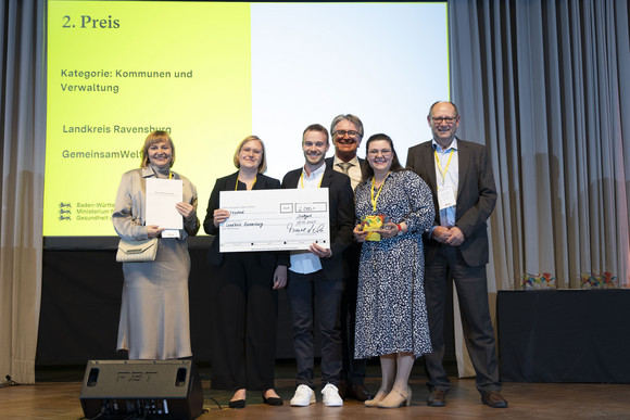 Preisverleihung Integrationspreis des Landes Baden-Württemberg Gruppenfoto der Preisträger von Platz 2 der Kategorie „Kommunen und Verwaltungen“ mit Minister Manne Lucha auf Bühne.