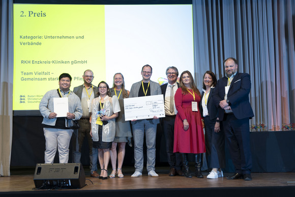 Preisverleihung Integrationspreis des Landes Baden-Württemberg Gruppenfoto der Preisträger von Platz 2 der Kategorie „Unternehmen und Verbände“ mit Minister Manne Lucha auf Bühne.