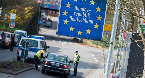 Polizisten kontrollieren französisches Fahrzeug, darüber Straßenschild mit Aufschrift „Bundesrepublik Deutschland“