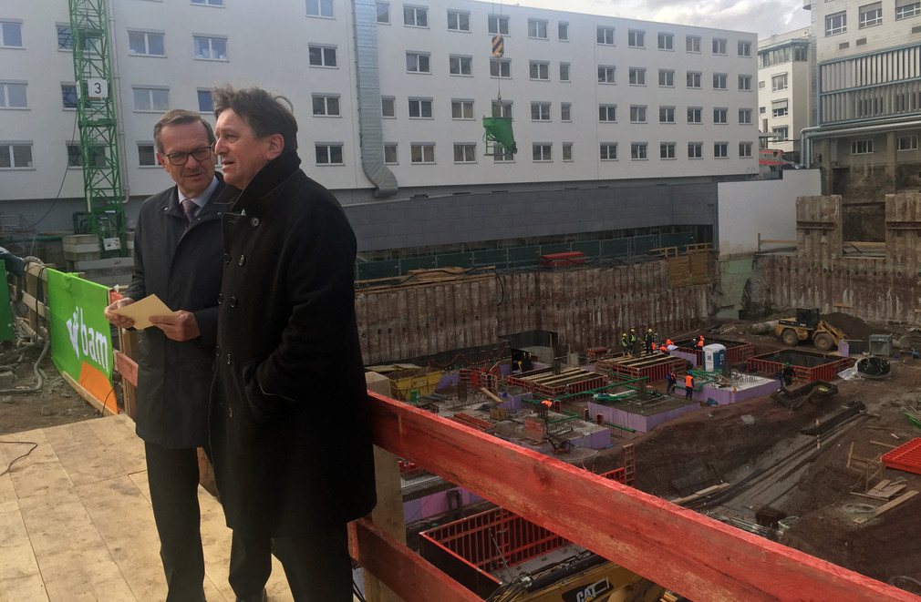 Gesundheitsminister Manne Lucha und Stuttgarts Oberbürgermeister Fritz Kuhn stehen am Rand der Großbaustelle