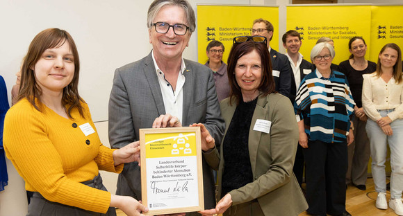 Sozialminister Manne Lucha posiert gemeinsam mit Preisträgern und ihrer Siegerurkunde.