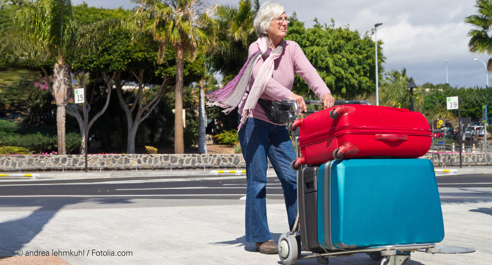 Ältere Frau steht mit Koffern an Bushaltestelle