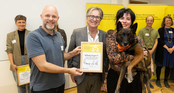 Sozialminister Manne Lucha posiert gemeinsam mit Preisträgern und ihrer Siegerurkunde.