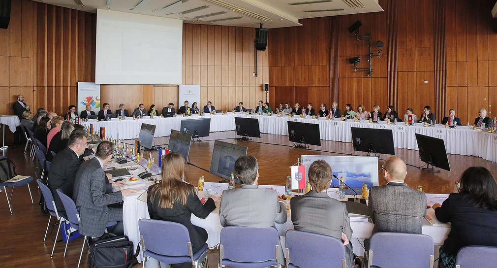 Teilnehmerinnen und Teilnehmer sitzen an rundem Konferenztisch