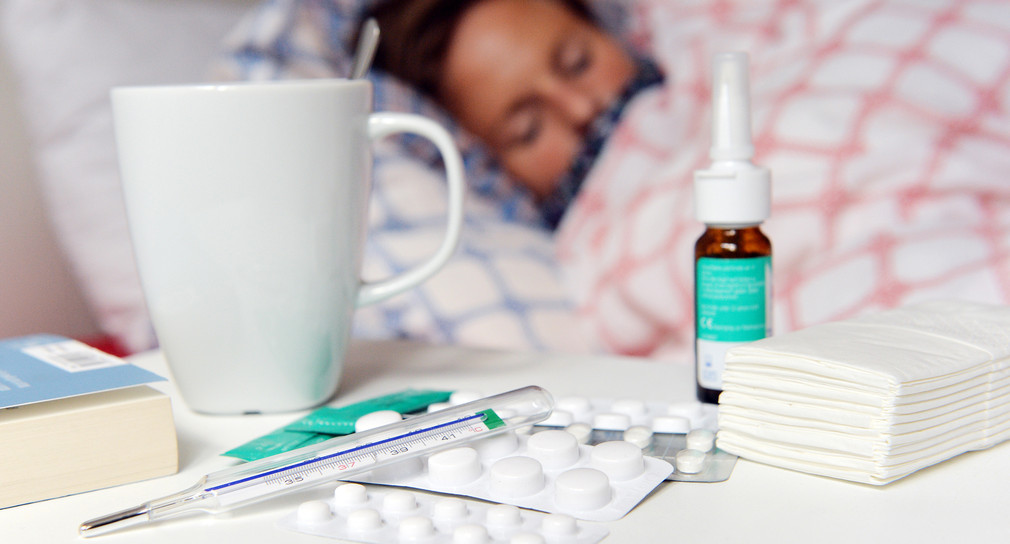 Kranke Frau im Bett und Medikamente und Fieberthermometer auf dem Nachttisch