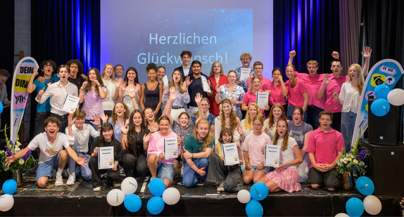Alle Preisträger und Preisträgerinnen des Jugendbildungspreises DeinDing 2025 haben sich mit ihren Urkunden auf der Bühne zum Gruppenbild versammelt. 