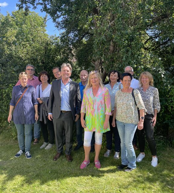 Gruppenfoto von Minister Lucha mit Verantwortlichen des Bürgertreffs Inzigkofen im Freien vor Obstbäumen.