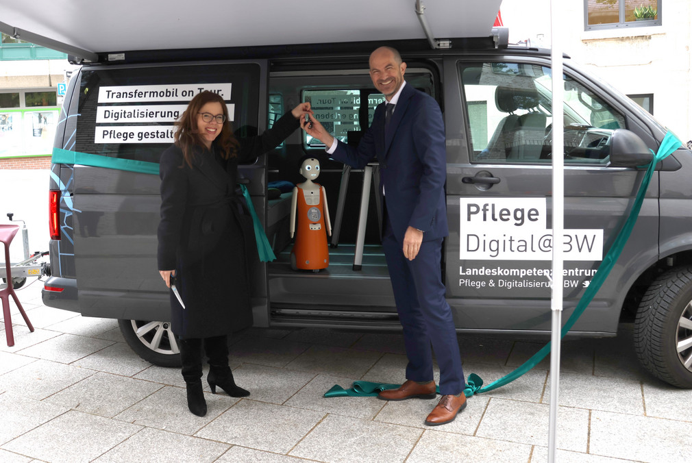 Ministerialdirektorin Leonie Dirks steht vor Transfermobil und übergibt Fahrzeugschlüssel an Prof. Dr. Daniel Buhr vom Landeskompetenzzentrum Pflege & Digitalisierung.