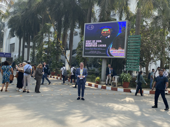 Minister Manne Lucha steht in Navi Mumbai im Freien vor einer großen Werbeleinwand, auf der sein Bild und sein Name zu sehen sind.