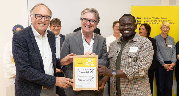 Sozialminister Manne Lucha posiert gemeinsam mit Preisträgern und ihrer Siegerurkunde.