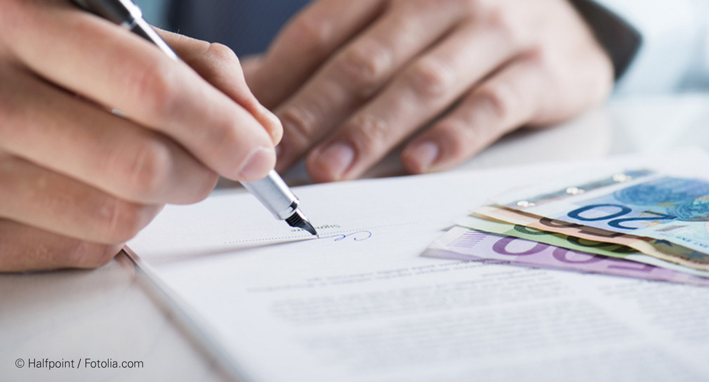 Mann unterzeichnet Vertrag mit Geldstapel daneben