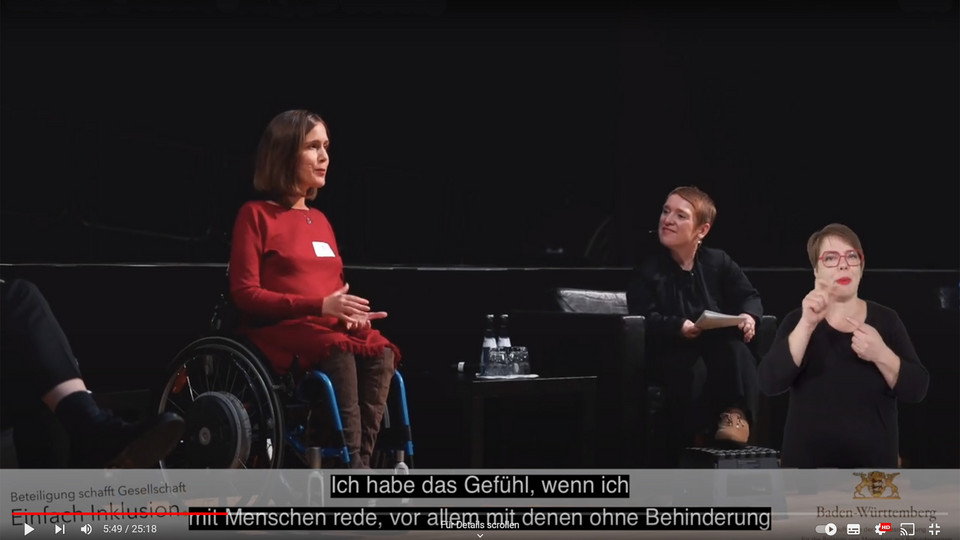 Simone Fischer moderiert Veranstaltung und spricht mit weiblichem Gast auf der Bühne.