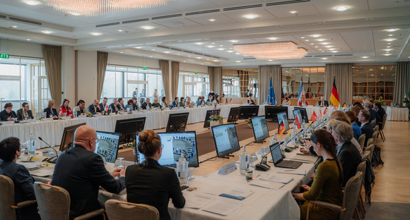 Kompletter Blick auf viereckigen Konferenztisch mit allen Teilnehmenden der Integrationsministerkonferenz.