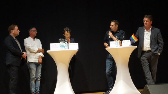 Grußwort/Podium CSD-Empfang der Landesregierung Beim Podiumsgespräch auf der Bühne ging es um die Schwierigkeiten und Erfolge beim Kampf für Akzeptanz und gleiche Rechte.
v.l.n.r.: Karl Moehl, Referatsleiter der Antidiskriminierungsstelle des Bundes, Michael Frech, Vorstand des CSD Ulm.Neu-Ulm, Adrienne Braun, Christoph Michl, Geschäftsführer IG CSD Stuttgart, Sozial- und Integrationsministeri Manne Lucha.