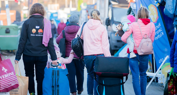 Geflüchtete Frauen und Kinder werden an einem Grenzübergang von einer freiwilligen Helferin begleitet.