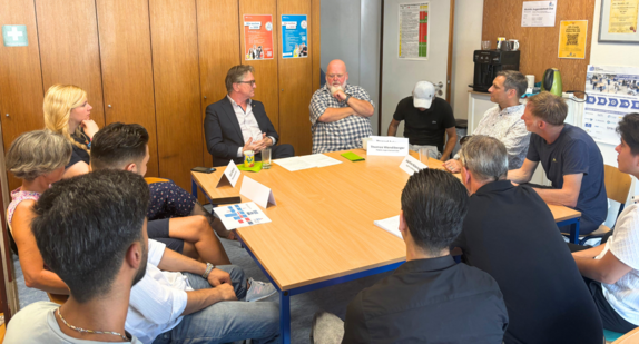 Minister Manne Lucha sitzt dem Team der Mobilen Jugendarbeit um einen Tisch und lässt sich das Konzept der aufsuchenden, stadtteilorientierten Arbeit erläutern.