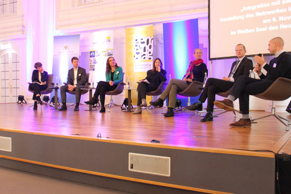 Podiumsdiskussion mit einzelnen Strategiegruppenmitgliedern des Netzwerkes Integration und der Leiterin der AG „Empowerment von Frauen mit Flucht- und Einwanderungsgeschichte“ sowie dem Leiter der AG „Demokratiebildung und politische Partizipation“ vor Publikum.