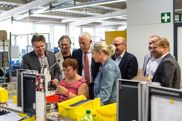 Oberbürgermeister Harry Mergel, Minister Manne Lucha, Ursel Wolfgramm (Deutscher Paritätischer Wohlfahrtsverband Landesverband BW) und Martina Wieland (Geschäftsführerin Therapeutikum) schauen einer Werkstattarbeiterin bei der Arbeit zu