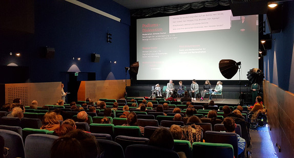 Publikum in Kinosaal verfolgt Podiumsdiskussion von Teilnehmenden der Veranstaltung „Rette sich, wer kann?!“, darunter Landes-Beauftragte Simone Fischer und Innenminister Thomas Strobl. 