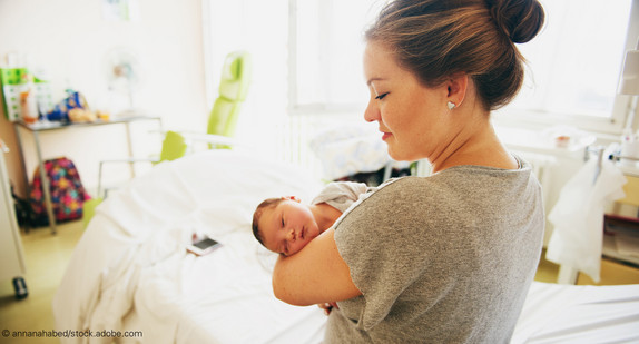 Frau mit Neugeborenem sitzt auf Bett