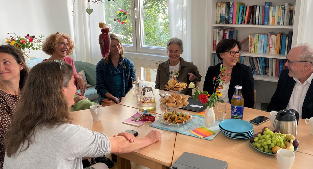 Staatssekretärin Dr. Ute Leidig sitzt mit Verantwortlichen des Mehrgenerationenhauses in Heidenheim um einem Tisch und lässt sich die Arbeit der Initiative erklären. Der Raum ist gemütlich eingerichtet und dekoriert. Auf dem Tisch stechen Getränke und Snacks.