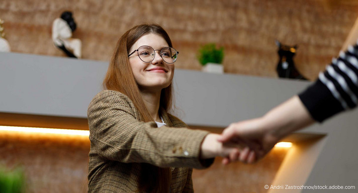 Lächelnde junge Frau gibt anderer Person in Büro die Hand.