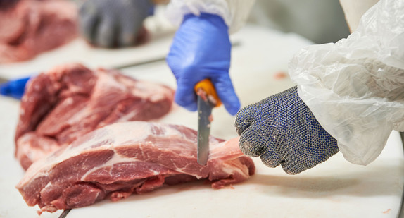 Mitarbeiter eines Schlachtbetriebs zerlegt ein Stück Fleisch