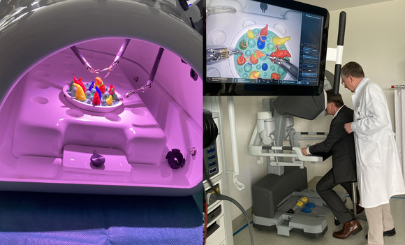 Minister Lucha sitzt vor einem Operationsroboter. Ein Arzt vom Siloah St. Trudpert Klinikum schaut ihm über die Schulter.