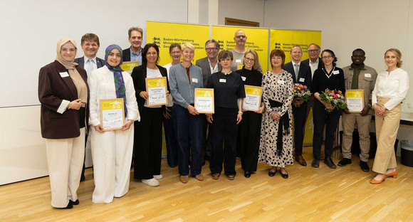 Gruppenfoto: Wettbewerbsjury und Minister Manne Lucha gemeinsam mit mehreren Preisträgern und deren Siegerurkunden.