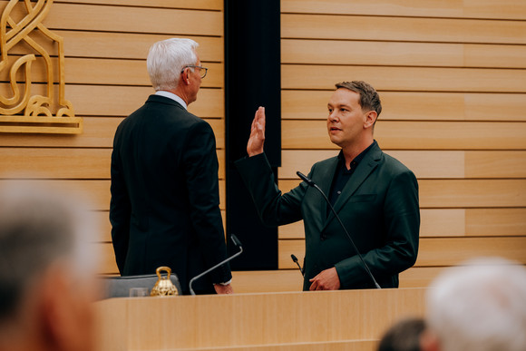 Oliver Hildenbrand steht auf der Tribüne des Landtags Baden-Württemberg mit erhobener Hand vor Landtagspräsident Thomas Strobl.