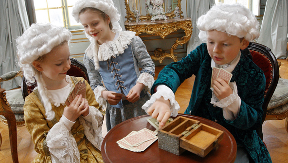 Kinder in Barock-Kostümen spielen Karten